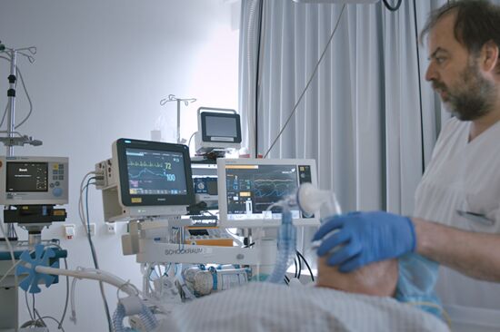 Ein Arzt am Bett eines beatmeten Patienten, im Hintergrund Überwachungsmonitore Ein Arzt am Bett eines beatmeten Patienten, im Hintergrund Überwachungsmonitore