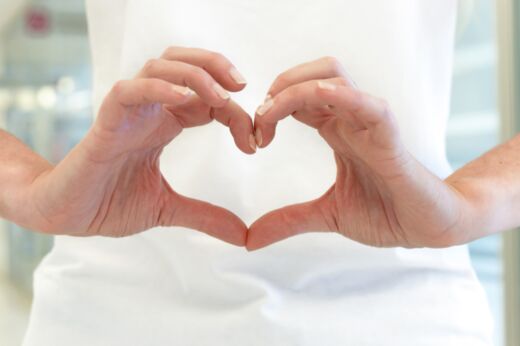 Schmuckbild: Zwei Hände formen ein Herz vor dem Rumpf einer Person in weißer Krankenhaustracht