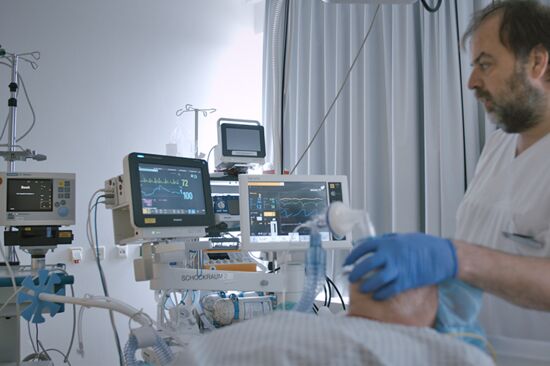 Ein Arzt am Bett eines beatmeten Patienten, im Hintergrund Überwachungsmonitore