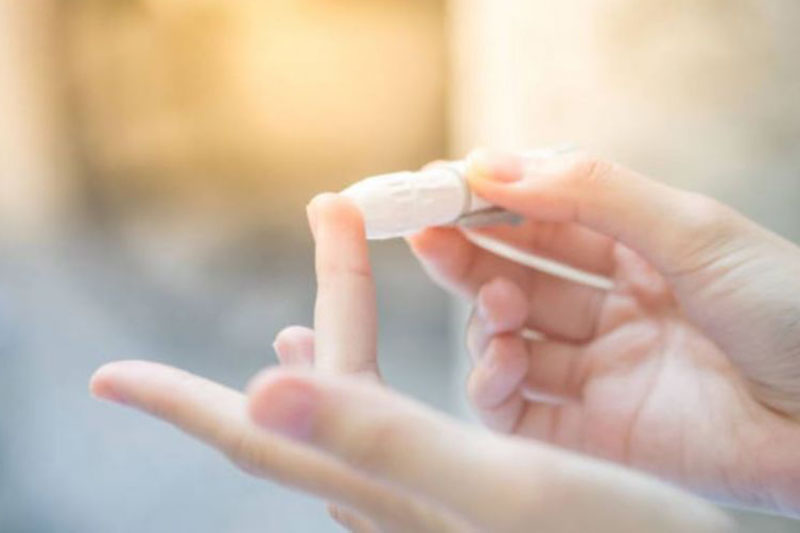 Nahaufnahme von Händen mit Lanzette auf Finger, um eine Probe für die Messung am Blutzuckermessgerät zu nehmen; verlinkt zur Seite der 'Praxis für Diabetologie'
