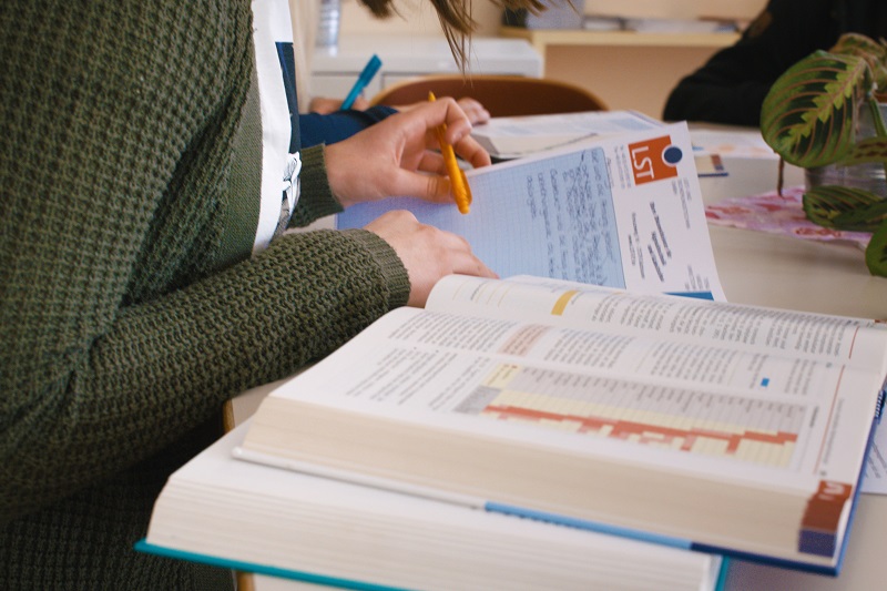 Schmuckbild: Schreibtisch, Lehrbücher, Notizblock und Hände einer Frau beim Lernen