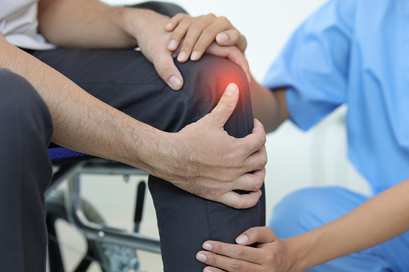 Schmuckbild: eine Ärztin untersucht das schmerzende Knie eines Patienten, der sein Bein mit den Händen festhält