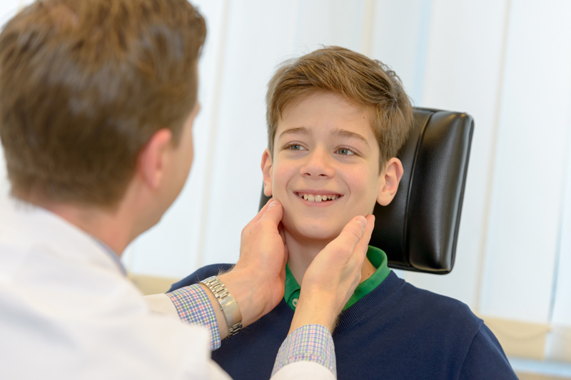 Ein Hals-Nasen-Ohrenarzt tastet den Hals eines jugendlichen Patienten ab; verlinkt zur Seite der 'Praxis für Hals-, Nasen-, Ohrenheilkunde'