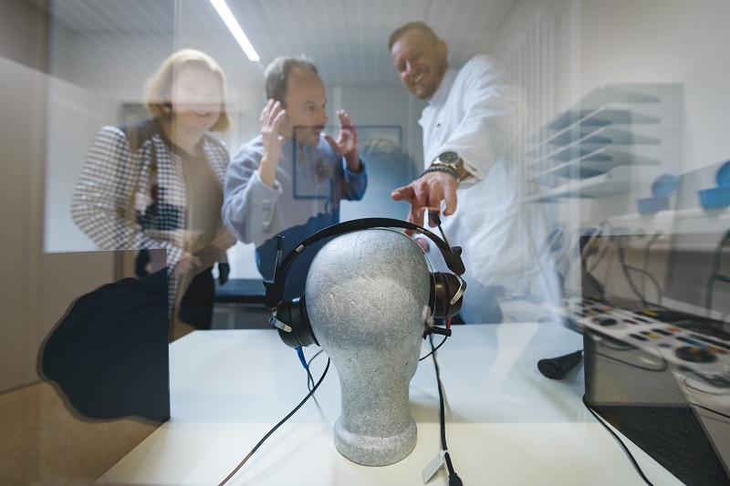 Ein Arzt erklärt einem Ehepaar ein Gehör-Messystem in Form eines Kopfhörers auf einem Styroporkopf