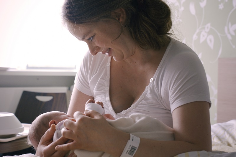 Szenenfoto von der Wöchnerinnenstation: Eine Mutter hält ihr Neugeborenes im Arm