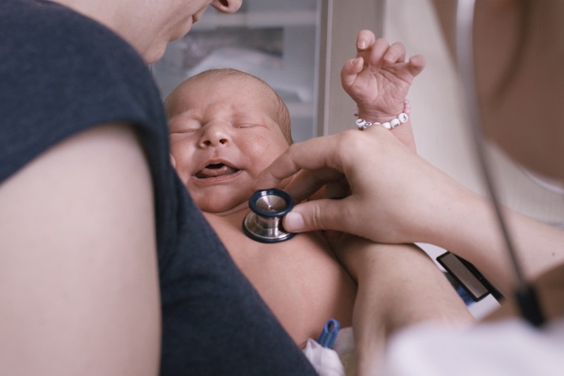 Bei einem Neugeborenen wird mit einem Stethoskop der Brustkorb abgehört