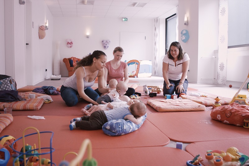 mehrere Mütter spielen mit ihren Kleinkindern auf Bodenmatten und Kissen; verlinkt zum 'Eltern-Kind-Zentrum'