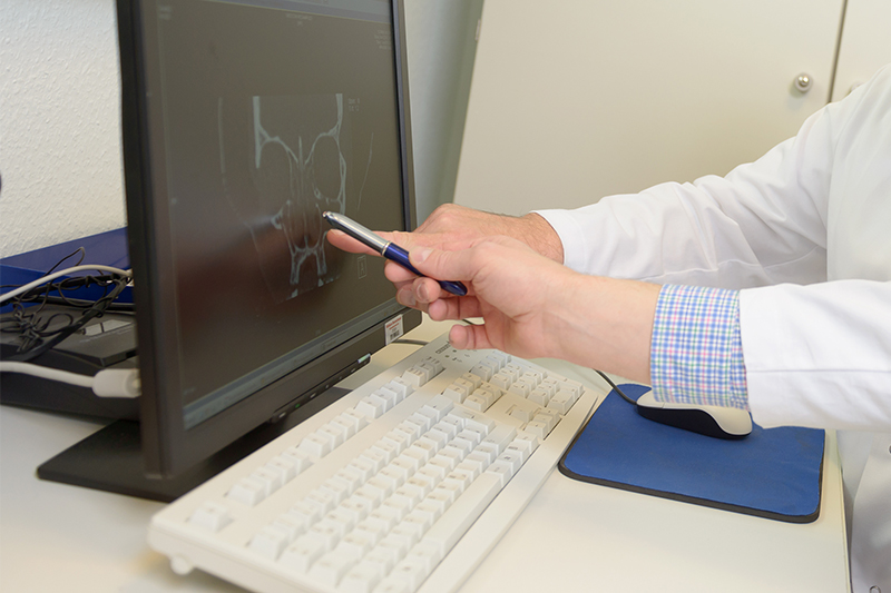 zwei Hände zeigen auf einen Laptopmonitor mit Röntgenbild eines Schädels