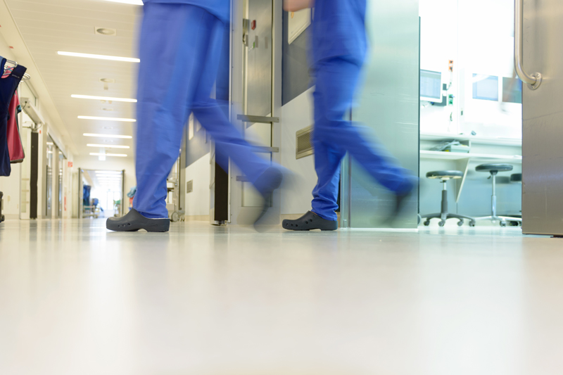 Zwei Paar Beine in OP-Schutzkleidung verlassen eilig ein Krankenhauszimmer; verlinkt zur Seite der 'Praxis für Chirurgie'