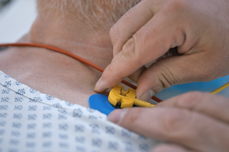 Schmuckbild: Hände, die eine Elektrode am Halsansatz eines Patienten anbringen; verlinkt zu 'Klinik für Akut- und Notfallmedizin'