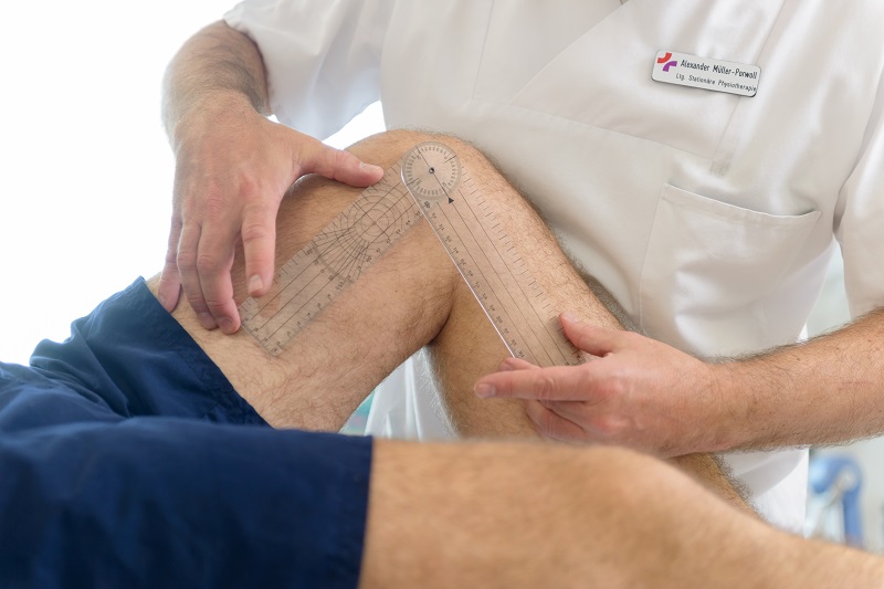 ein Physiotherapeut misst den Winkel am gebeugten Knie eines Patienten