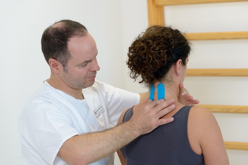 ein Physiotherapeut behandelt Halswirbelsäule einer Patientin, deren Nacken mit Knesiotape versehen ist