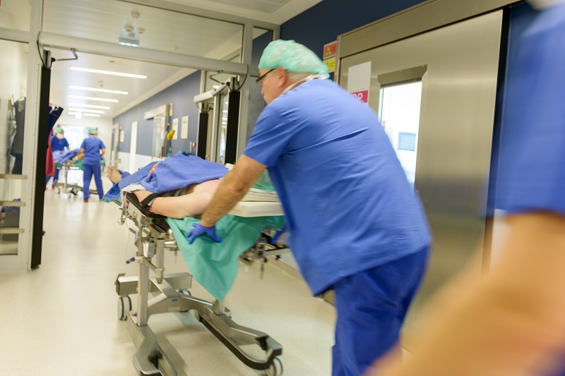 Pfleger fahren Patienten auf OP-Liegen zum Operationsbereich; verlinkt zur Seite der 'Praxis für Gefäßchirurgie'
