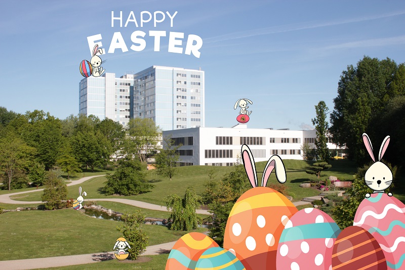 Bild des Klinikums mit eingefügten Zeichnungen von Osterhasen und Ostereiern und dem Schriftzug "Happy Easter"