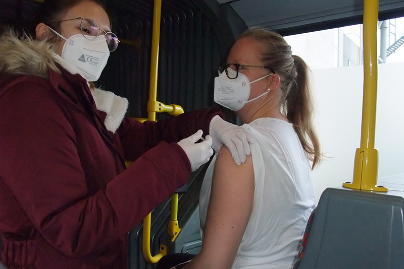 Szenenfoto aus dem Impfbus: Eine Mitarbeiterin des Werksarztzentrums injiziert einer Frau den Impfstoff in den linken Oberarm