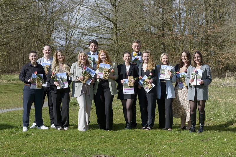 Dreizehn Absolventen und Absolventinnen der Pflegeakademie mit ihren Berufsurkunden und einer Blume (Foto: Schimanke)