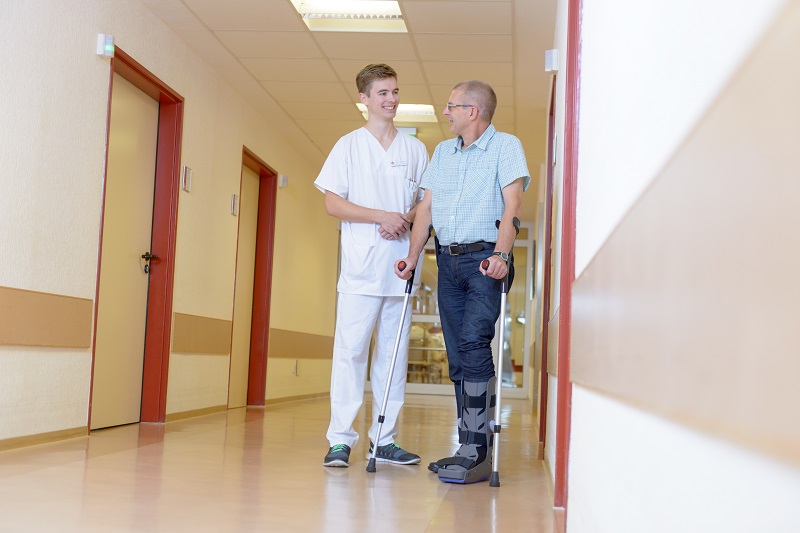 ein Pfleger im Gespräch mit einem Patienten, der mit orthopädischem Stiefel und Gehstützen steht (Foto: Antje Schimanke)