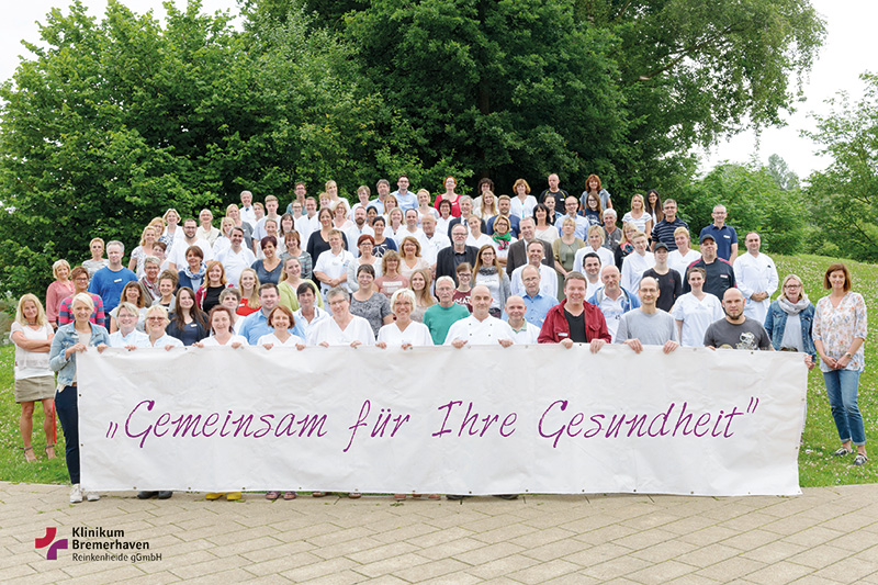 Gruppenbild von Mitarbeiterinnen und Mitarbeitern des Klinikums Bremerhaven-Reinkenheide hinter einem Banner mit der Aufschrift "Gemeinsam für Ihre Gesundheit"
