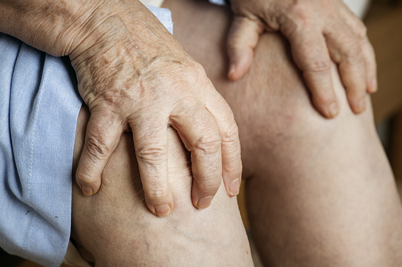 Schmuckbild: Die Knie einer älteren Person, die mit jeder Hand eines ihrer Knie festhält (Quelle: rawpixel.com auf Freepik)